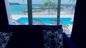 A room with a view of a pool and beach, featuring a sofa and patterned cushions. - Thalassa Beach and Pool Villa (Yoron)