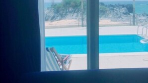 A view from a window of a swimming pool with a clear sky and palm trees. - Thalassa Beach and Pool Villa (Yoron)