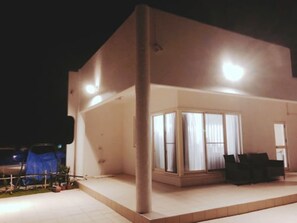 A modern building with a large glass windowed section, a flat roof, and a small outdoor seating area with chairs. - Thalassa Beach and Pool Villa (Yoron)