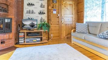 A cozy cabin interior with a fireplace, a television, a sofa, and a wall decorated with maritime-themed artwork.