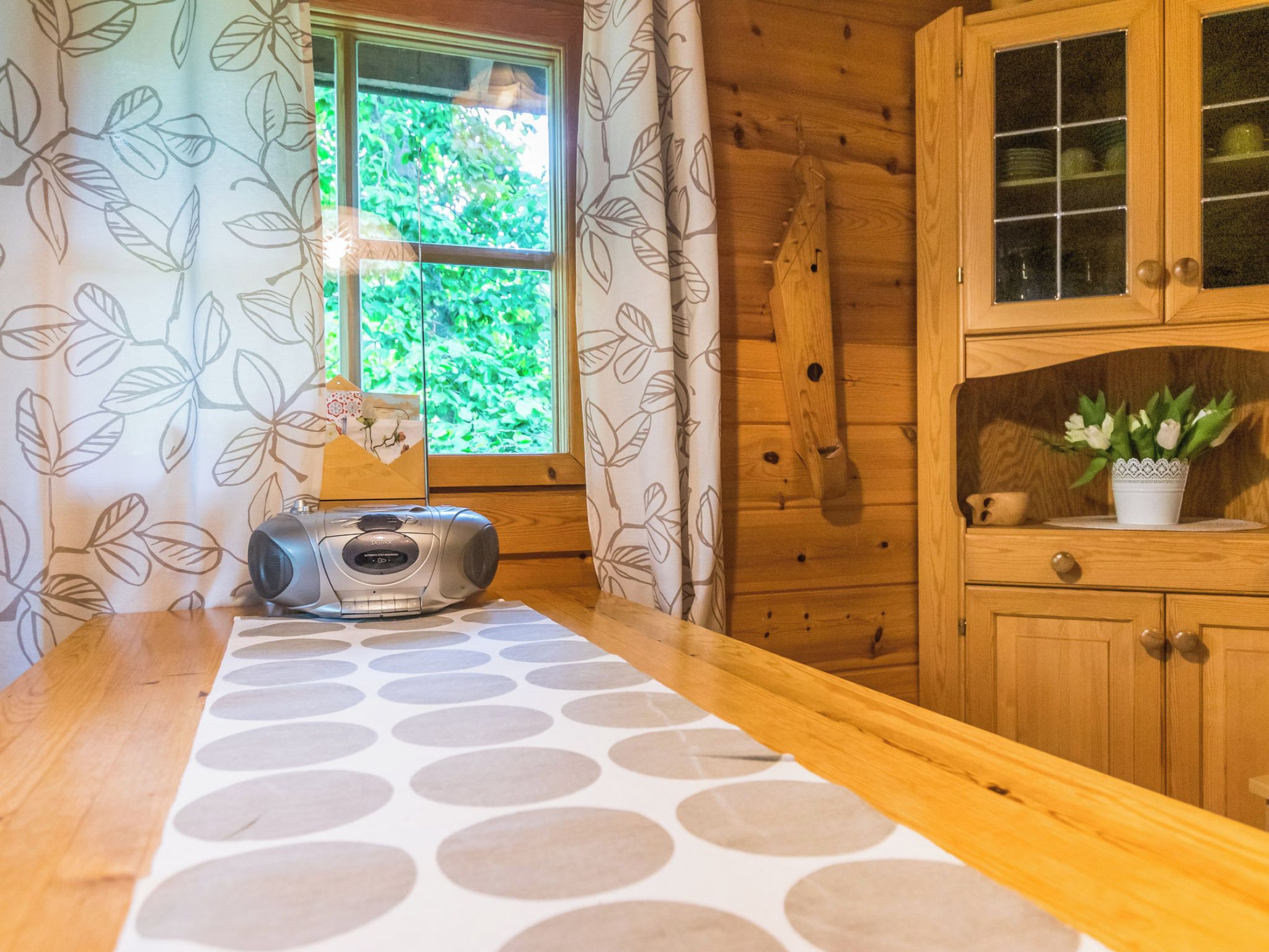 A wooden cabin interior with a kitchen area, a window with a view of greenery, and a radio on the counter.