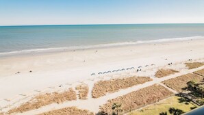 A beach with a clear sky, sandy shore, and a few people. There are pathways and some vegetation in the foreground. - Beautiful Oceanfront, Full Kitchen, Pet Friendly (Myrtle Beach)