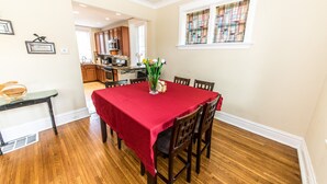 Uma sala de jantar com toalha de mesa vermelha, cadeiras de madeira e um vaso com flores.