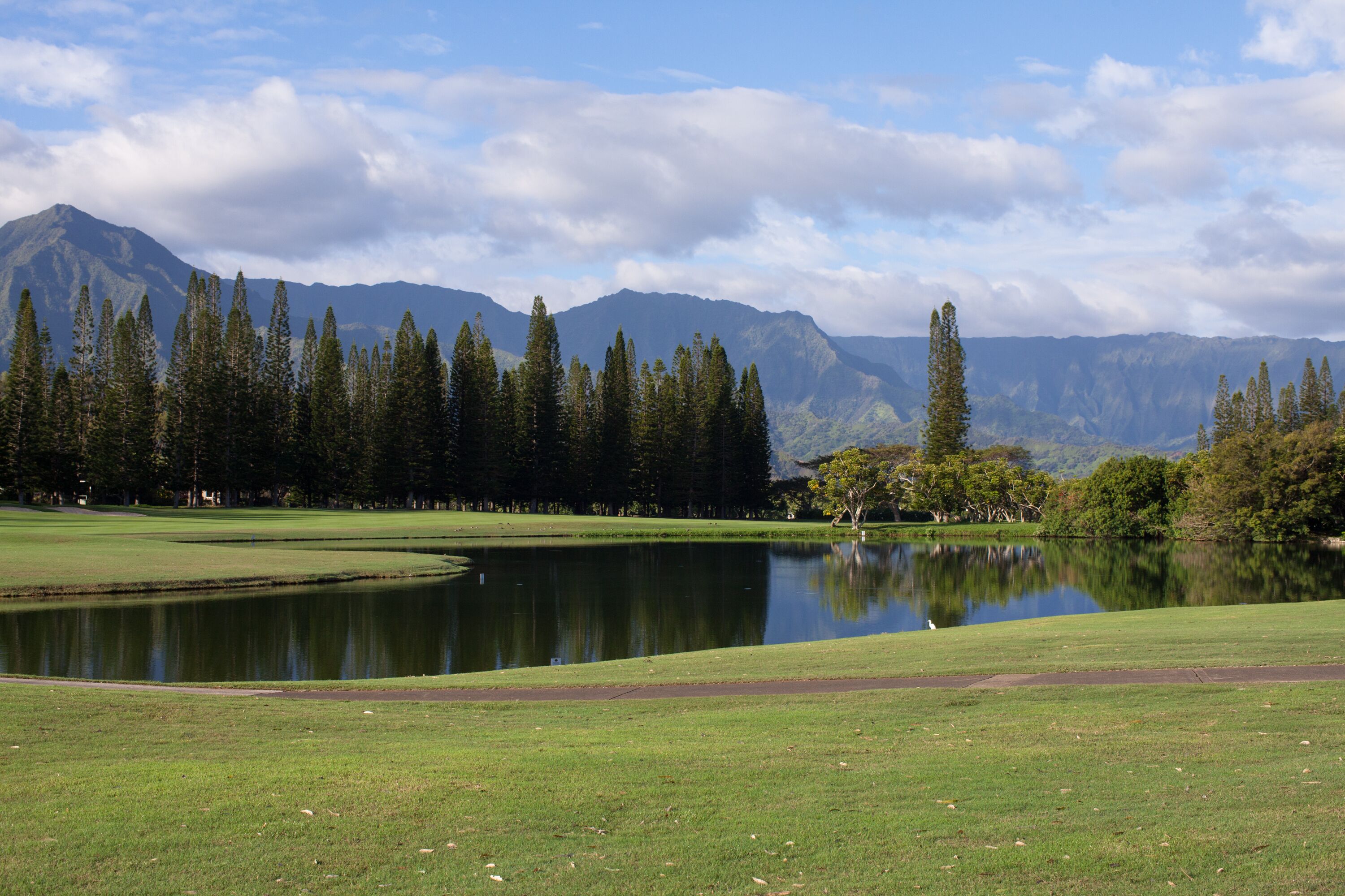 Un paysage paisible avec un lac, un terrain de golf et des montagnes en arrière-plan.