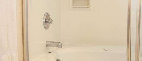 A bathroom with a bathtub, a shower, and a small shelf.