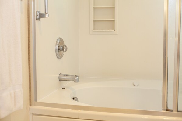 A bathroom with a bathtub, a shower, and a small shelf.