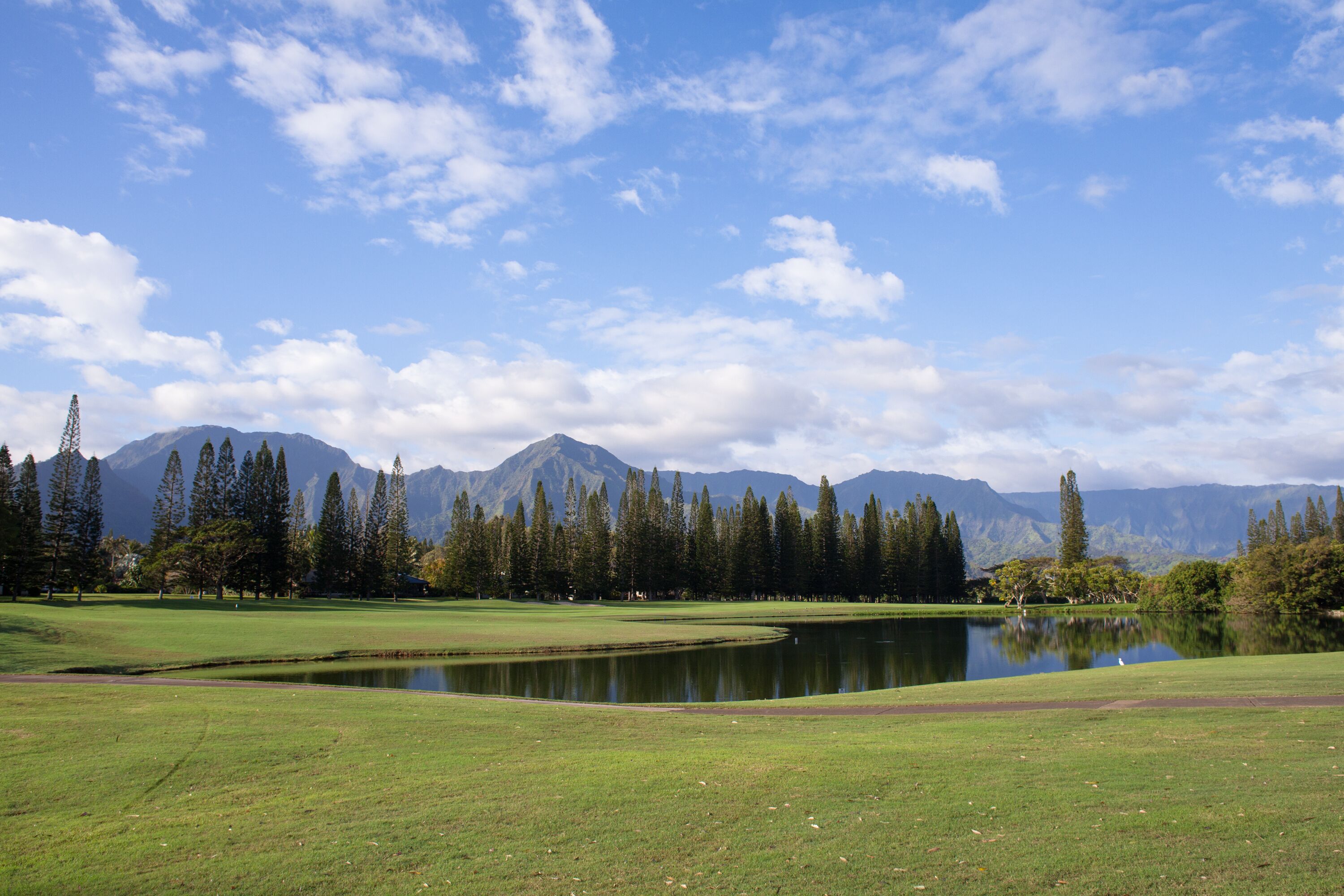 A golf course with a pond, trees, and mountains in the background.