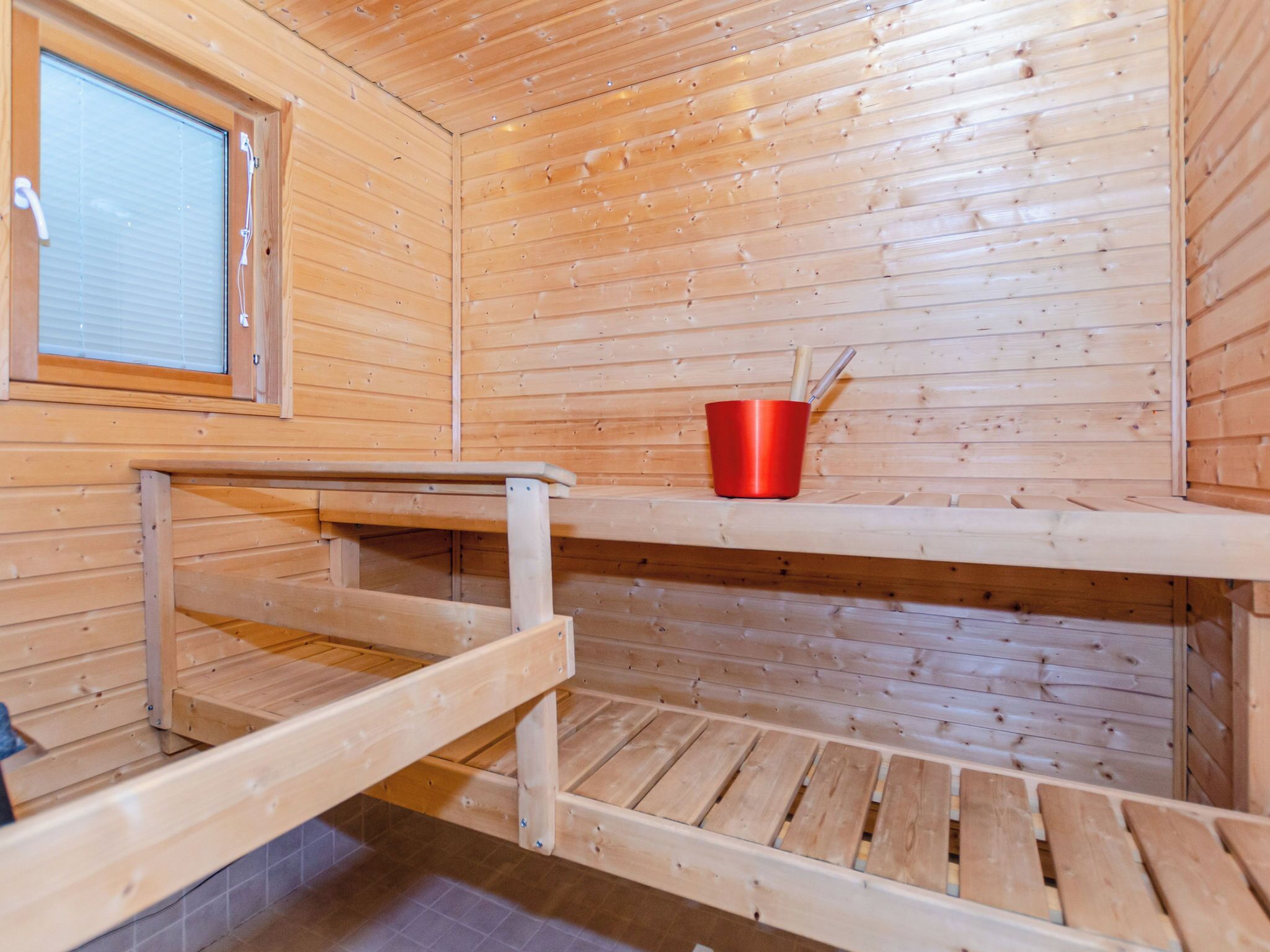 Una sauna con pareti in legno, una panchina e un secchio rosso.