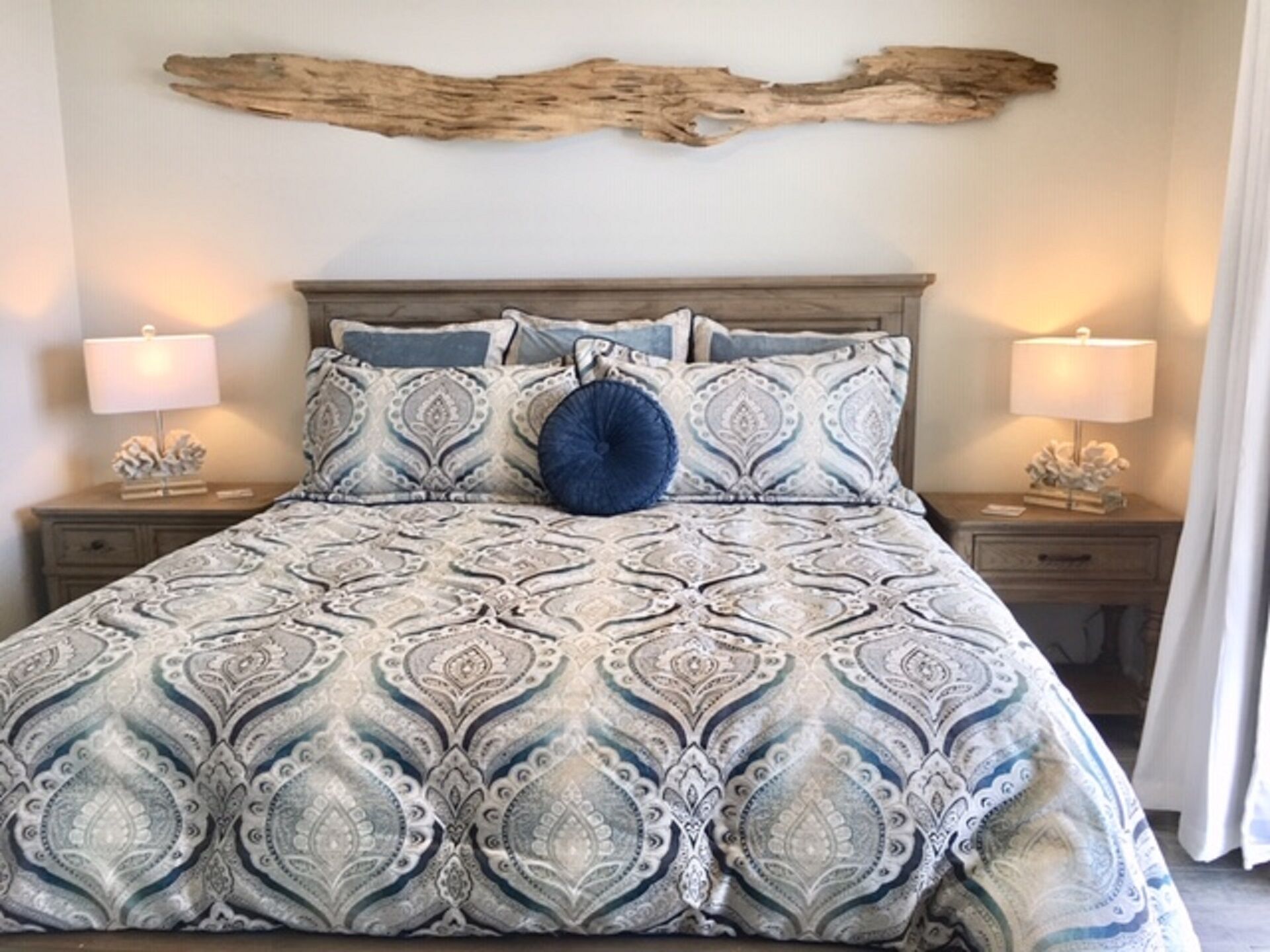 A bed with a patterned bedspread, two bedside tables with lamps, and a piece of driftwood on the wall.