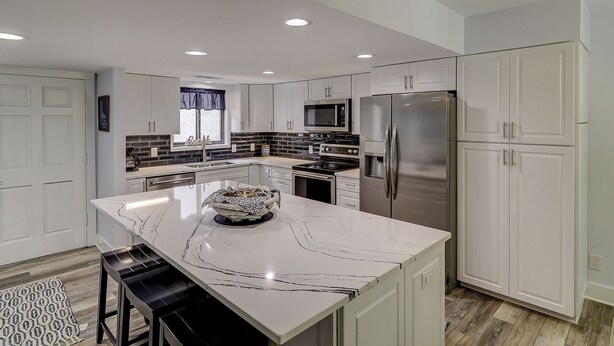 A modern kitchen with white cabinetry, a central island, stainless steel appliances, and a patterned rug.