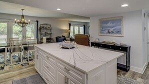 A spacious kitchen with a large island, recessed ceiling lights, and a dining area with chairs and a table.