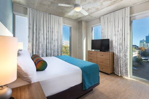 A hotel room with a bed, a television, a dresser, and large windows with curtains. - DOWNTOWN Austin with ROOFTOP Pool and BBQ Area, Fire Pit & a Fitness Center (Austin)