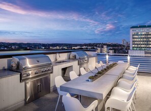 An outdoor kitchen with a grill, sink, and seating area on a rooftop with a city view. - DOWNTOWN Austin with ROOFTOP Pool and BBQ Area, Fire Pit & a Fitness Center (Austin)