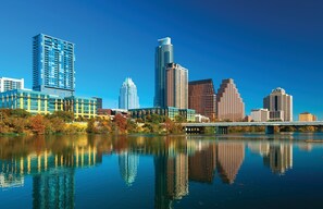 A city skyline with modern high-rise buildings, a river reflecting the structures, and a bridge crossing the river. - DOWNTOWN Austin with ROOFTOP Pool and BBQ Area, Fire Pit & a Fitness Center (Austin)