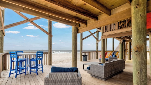 A wooden deck with wicker furniture, a table, and chairs overlooking the beach. - Livin the Dream - Beachfront, 6/6, POOL, Pet Friendly, Sleeps 15 (Dauphin Island)