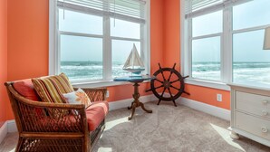 A room with a view of the ocean, featuring a wicker chair, a small table with a ship wheel, and a dresser. - Livin the Dream - Beachfront, 6/6, POOL, Pet Friendly, Sleeps 15 (Dauphin Island)