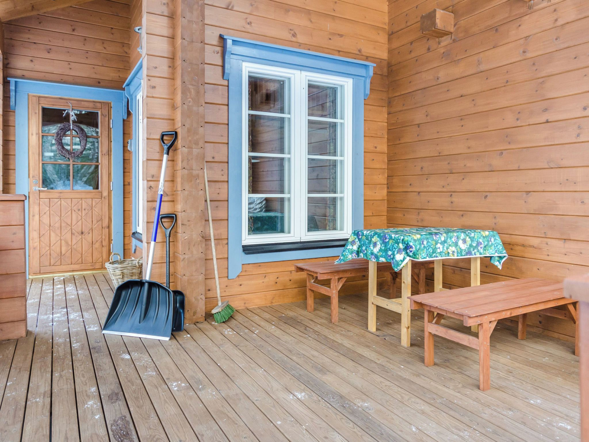 A wooden cabin with a porch, a table with a floral tablecloth, and various cleaning tools.