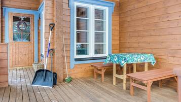 A wooden cabin with a porch, a table with a floral tablecloth, and various cleaning tools.