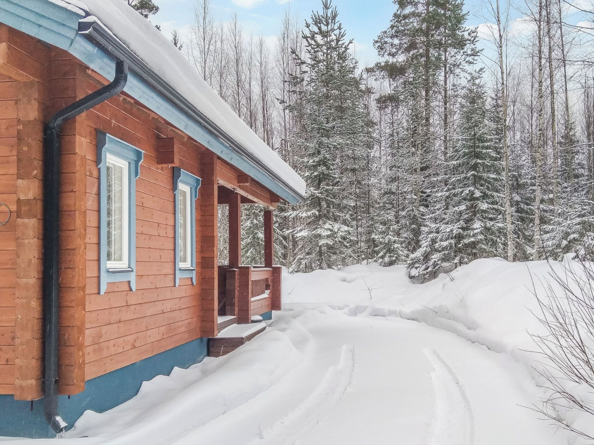 Uma cabana de madeira com varanda, rodeada por árvores cobertas de neve.