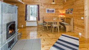 A cozy cabin interior with a fireplace, wooden walls, a dining area, and a window with curtains.