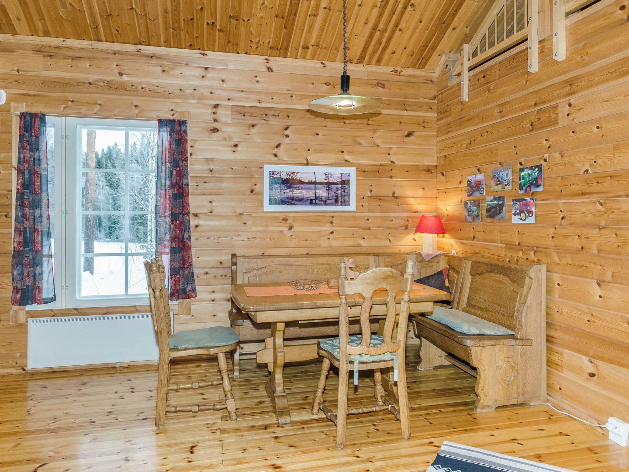 Un intérieur en bois comprenant une table à manger, des chaises, un banc, un luminaire suspendu et une fenêtre avec des rideaux.