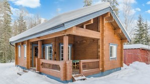 A wooden cabin with a porch, surrounded by snow.