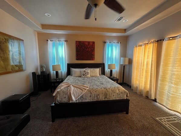 A bedroom with a large bed, two bedside tables with lamps, a ceiling fan, and curtains.