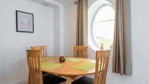A dining area with a round table, four wooden chairs, and a window with curtains. - Ferncourt Stepaside S (Dublin)