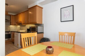 A compact kitchen with wooden cabinets, a microwave, and a dishwasher. There is a dining table with two chairs and a decorative vase. - Ferncourt Stepaside S (Dublin)