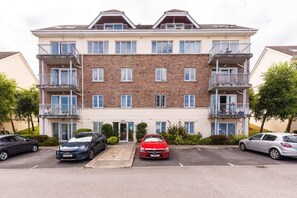 A multi-story residential building with a central entrance, balconies, and a parking area with cars. - Ferncourt Stepaside S (Dublin)