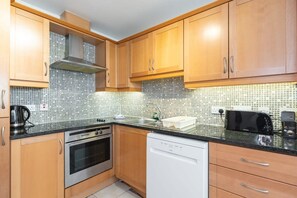 A kitchen with wooden cabinets, a stainless steel oven, a dishwasher, and a tiled backsplash. - Ferncourt Stepaside S (Dublin)