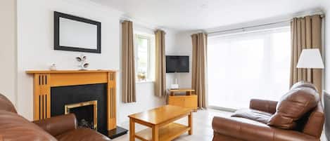 Una sala de estar con chimenea, sofás de cuero, una mesa de centro de madera y un televisor.