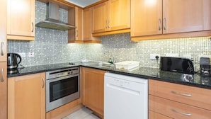 A compact kitchen with wooden cabinets, a tiled backsplash, a stove, an oven, a dishwasher, and a toaster. - Ferncourt Stepaside S (Dublin)