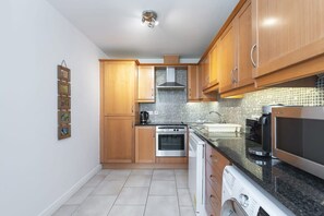 A modern kitchen with wooden cabinets, a stainless steel range hood, a built-in oven, a microwave, and a dishwasher. - Ferncourt Stepaside S (Dublin)
