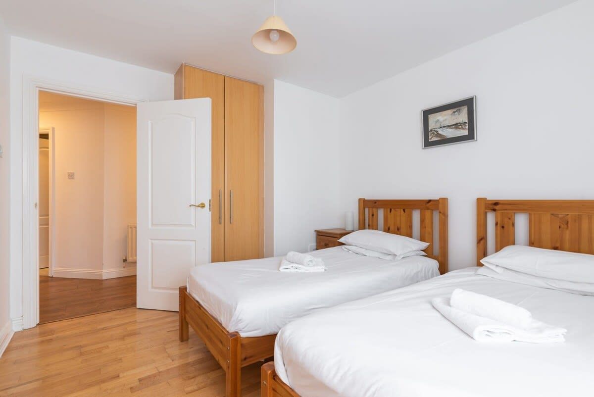A hotel room with two single beds, wooden headboards, a white door, and a framed picture on the wall.