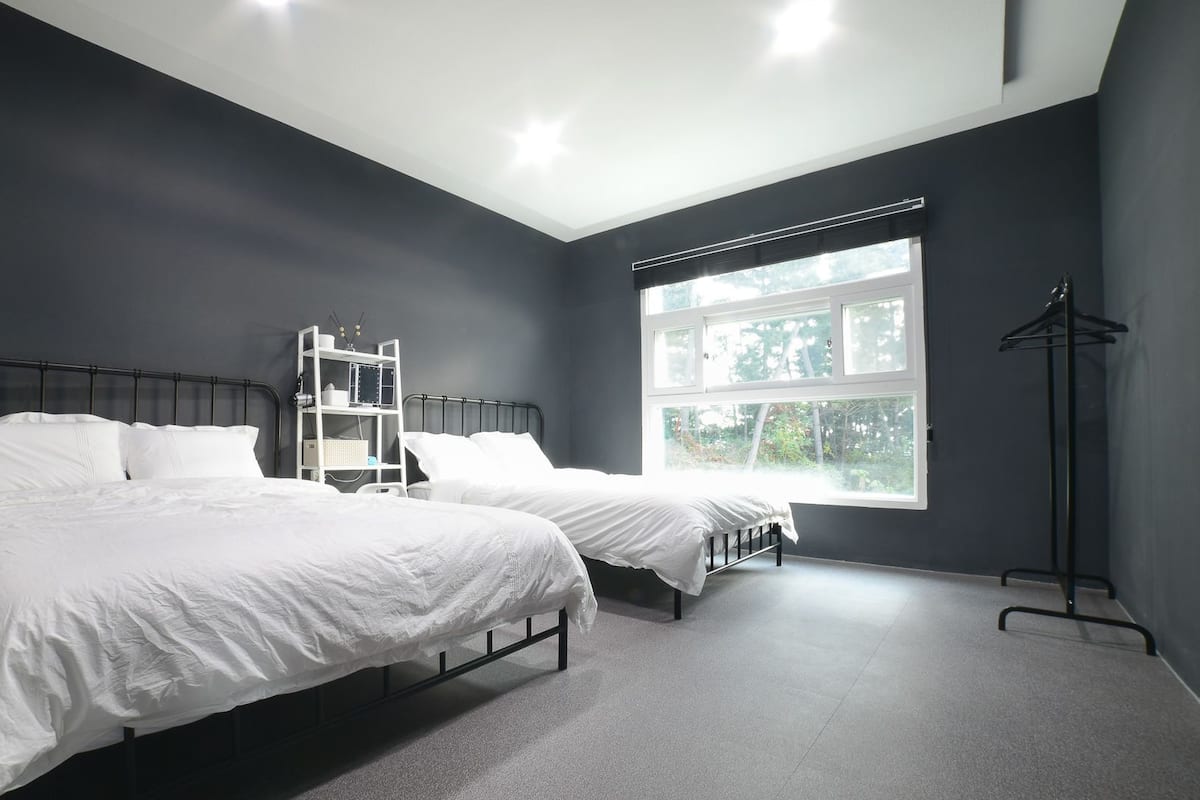 A bedroom with two beds, a white wardrobe, and a window with a view of trees.