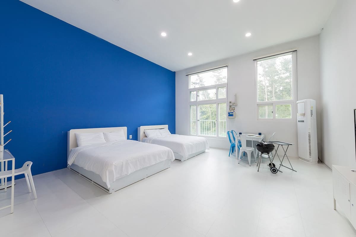 A hotel room with two beds, a desk, a chair, a TV, and a large window.