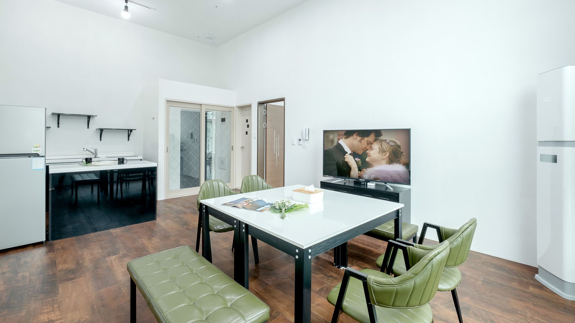 Una cuina moderna amb zona de menjador, una banca i un televisor que mostra una parella.