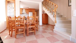 Un coin repas avec une table et des chaises en bois, une cuisine à l’arrière-plan et un escalier avec des rampes en bois.