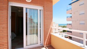 Un balcon avec une porte vitrée donnant sur une pièce, un mur en briques et une vue sur un immeuble doté de balcons.