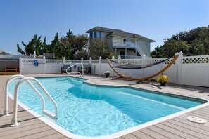 Une piscine avec une terrasse en bois, un hamac et une clôture blanche.