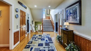 A hallway with wooden floors, a patterned rug, and a staircase leading to an upper level. - Coastal Castle: Pool, Dog-friendly, Separate Guest House, 530 Ft to Beach (Corolla)