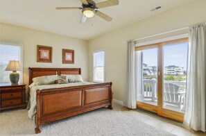 Une chambre avec un lit en bois, un ventilateur de plafond et une vue sur l’extérieur, accessible par une porte-fenêtre coulissante.