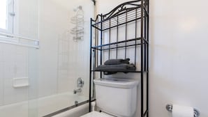 Ein Badezimmer mit Duschkabine aus Glas, Toilette und Ablage aus schwarzem Metall für Handtücher.