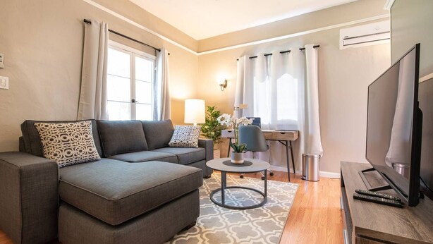 Ein modernes Wohnzimmer mit einem grauen Ecksofa, einem runden Couchtisch, einem Flachbildfernseher und einem Deckenventilator.