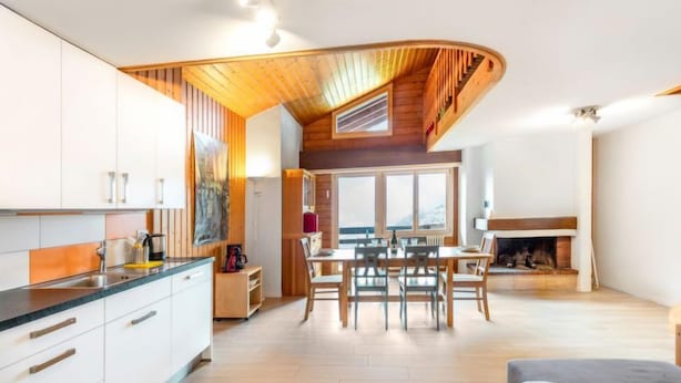 A modern kitchen with white cabinets, a wooden ceiling, and a dining area with a fireplace. - Centaure by Interhome (Sainte-Croix)