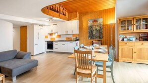 A modern kitchen with wooden cabinets, a dining area with a table set for four, and a living room with a sofa and a TV. - Centaure by Interhome (Sainte-Croix)