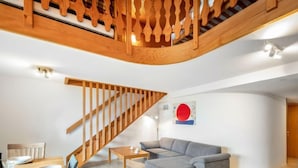 A modern living room with a wooden staircase, a grey sofa, and a dining table set for four. - Centaure by Interhome (Sainte-Croix)