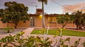 Una casa moderna con un césped cuidado, una palmera alta y diversos arbustos.