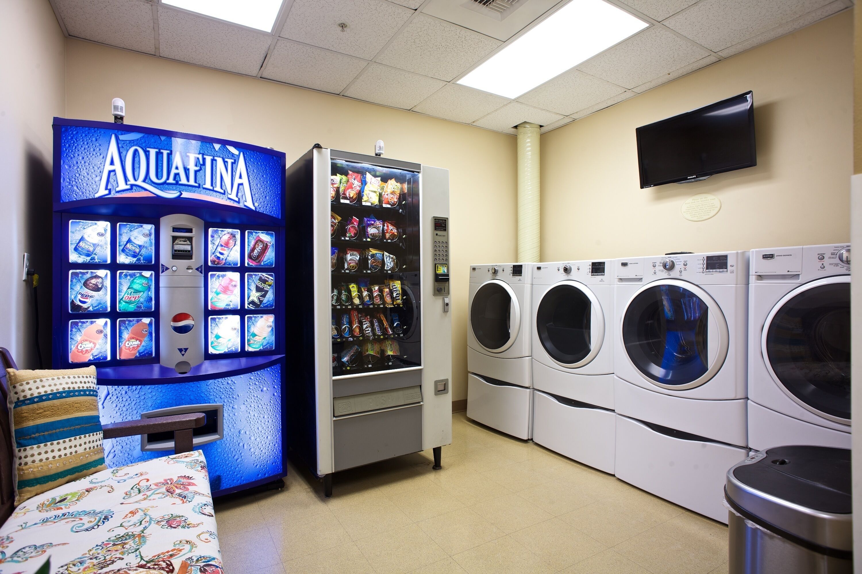 Une laverie équipée d’un distributeur automatique portant l’inscription « Aquafina » et de plusieurs machines à laver.